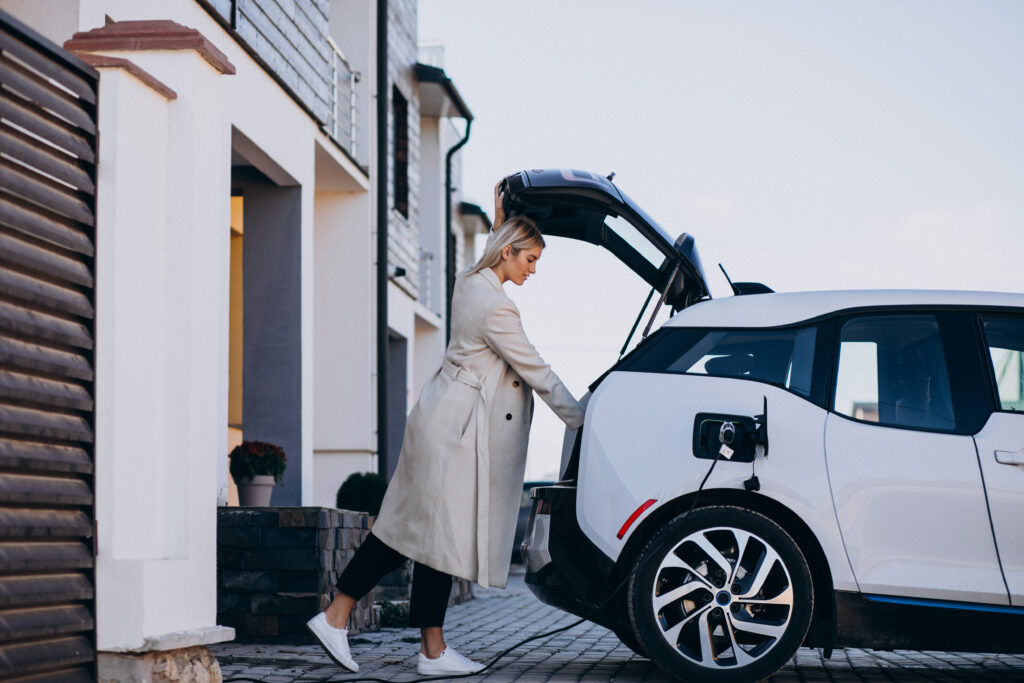 Woman beside an electric car charging in a residential driveway.