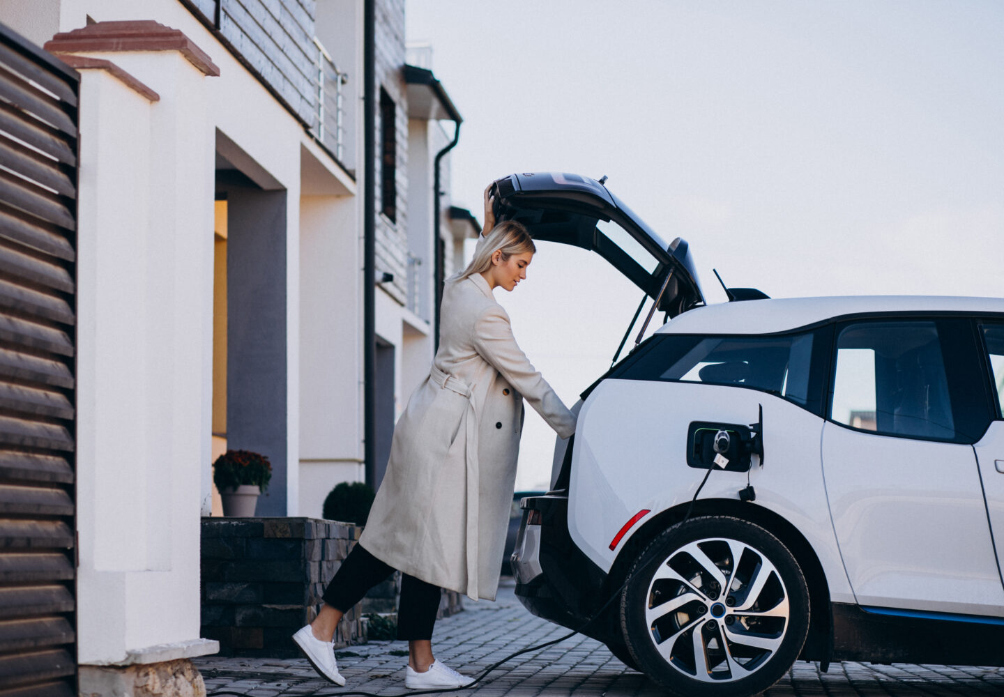 Woman beside an electric car charging in a residential driveway.