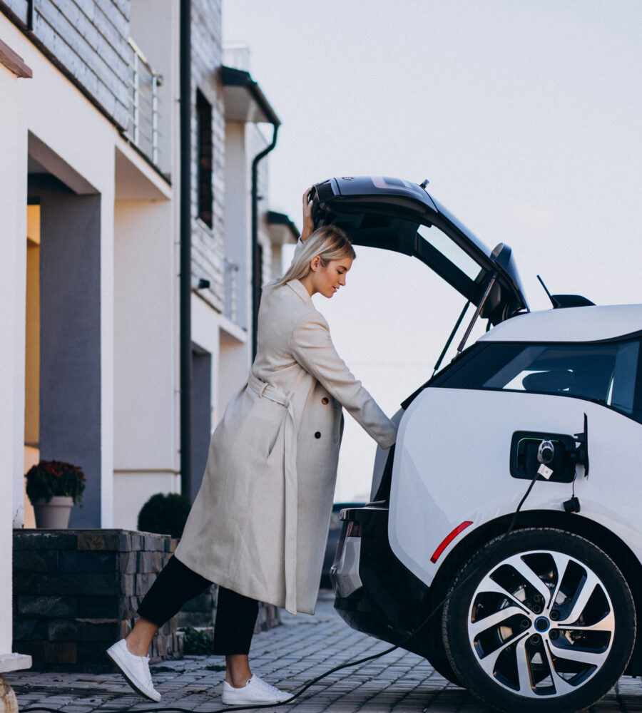 Woman beside an electric car charging in a residential driveway.