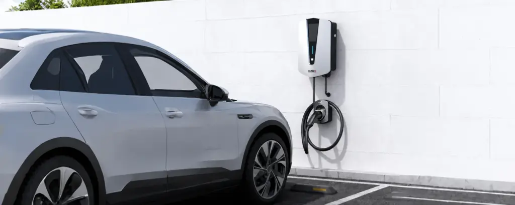 QIAO wall-mounted EV charger beside a parked car in an outdoor parking space.
