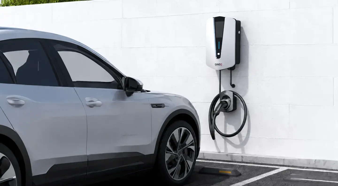 QIAO wall-mounted EV charger beside a parked car in an outdoor parking space.