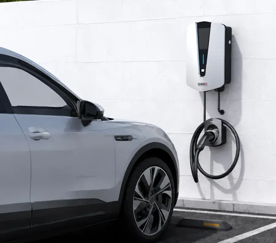 QIAO wall-mounted EV charger beside a parked car in an outdoor parking space.